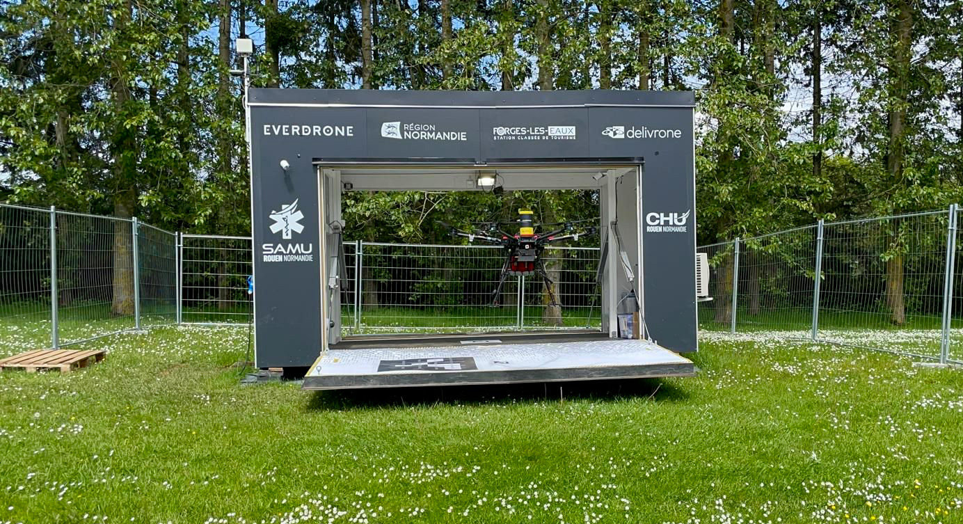 Photo montrant le drone de livraison de défibrillateur de Delivrone décollant depuis sa station. Cette dernière est de forme rectangulaire avec deux larges portes ouvertes de part de d'autre de sa longueur.