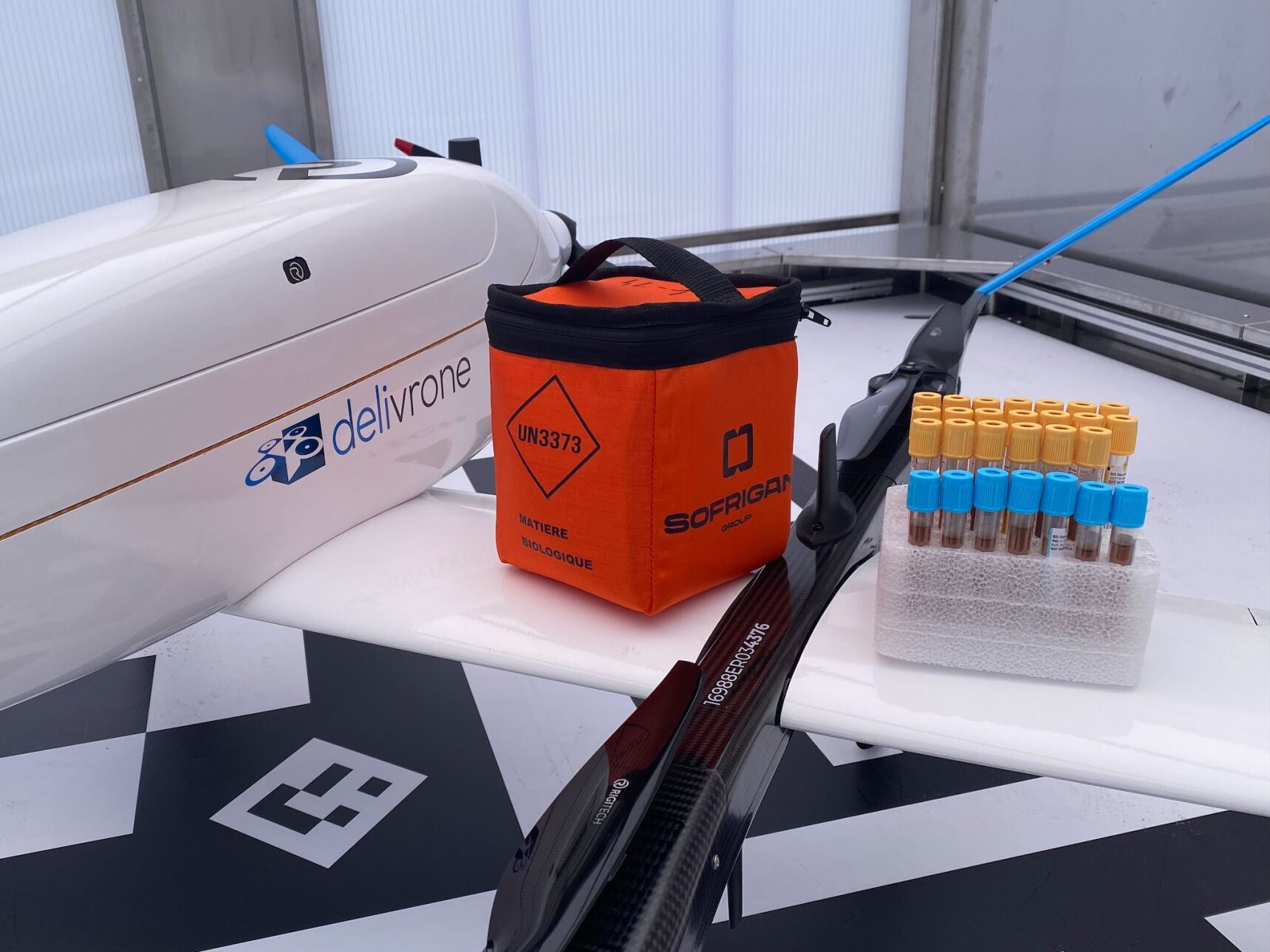 Photographie montrant un drone de transport médical sur l'aile duquel sont posées une sacoche et une boîte d'échantillons sanguins